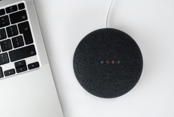 an overhead picture of a Apple Air laptop and a Google Home mini smart device on a white desk
