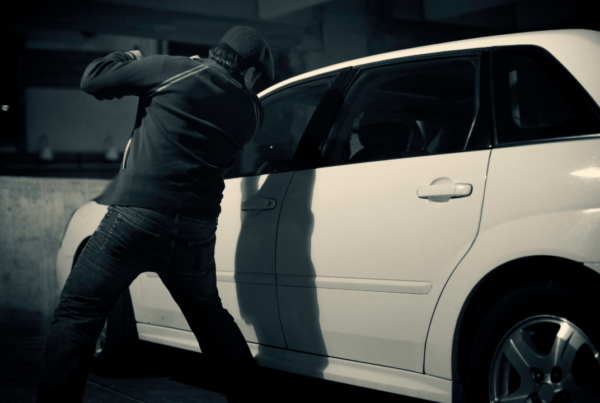 man breaking into a white car at night illustrating auto theft in Canada