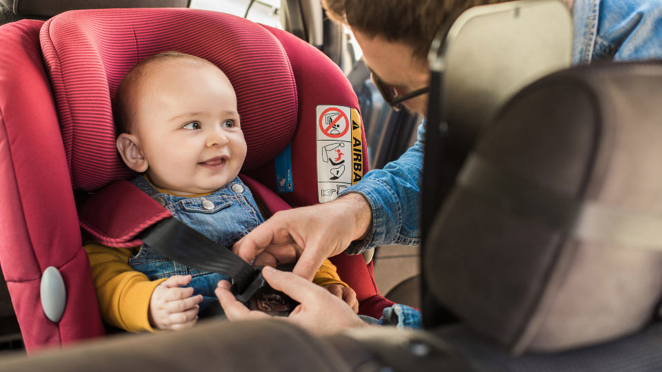 Father securing a happy baby in a car seat, showcasing child safety as part of mandatory insurance in Newfoundland and Labrador.