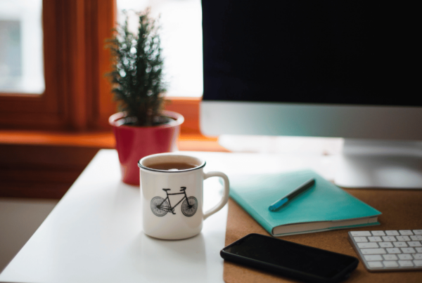 A cozy home office setup with a view of a window, displaying a white mug adorned with a bicycle illustration on a desk, alongside a notepad, pen, and smartphone, symbolizing the planning of home insurance costs in Newfoundland.
